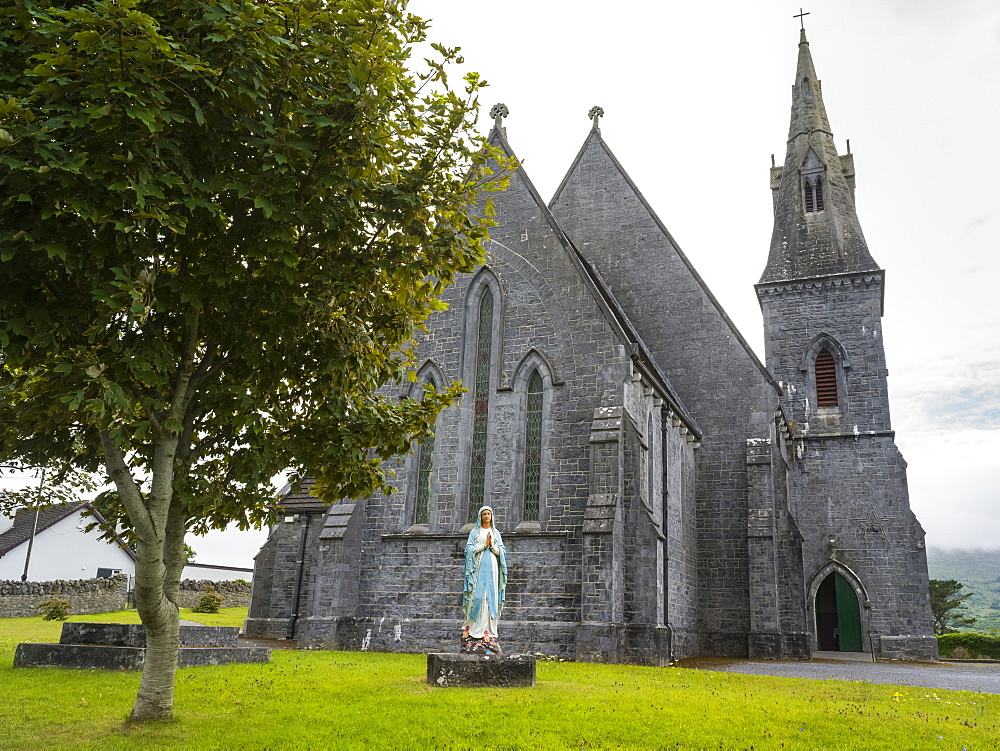 Stone church with bell tower and statue of praying woman in front, County Clare, Ireland