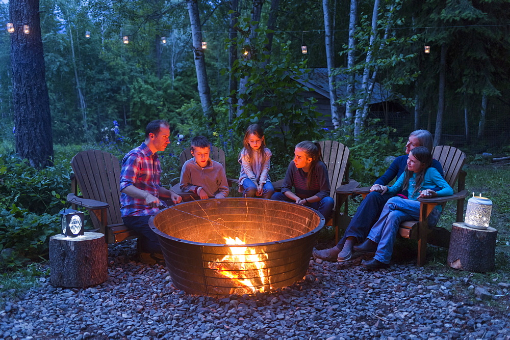 A family gathers outside around a campfire at dusk, Salmon Arm, British Columbia, Canada