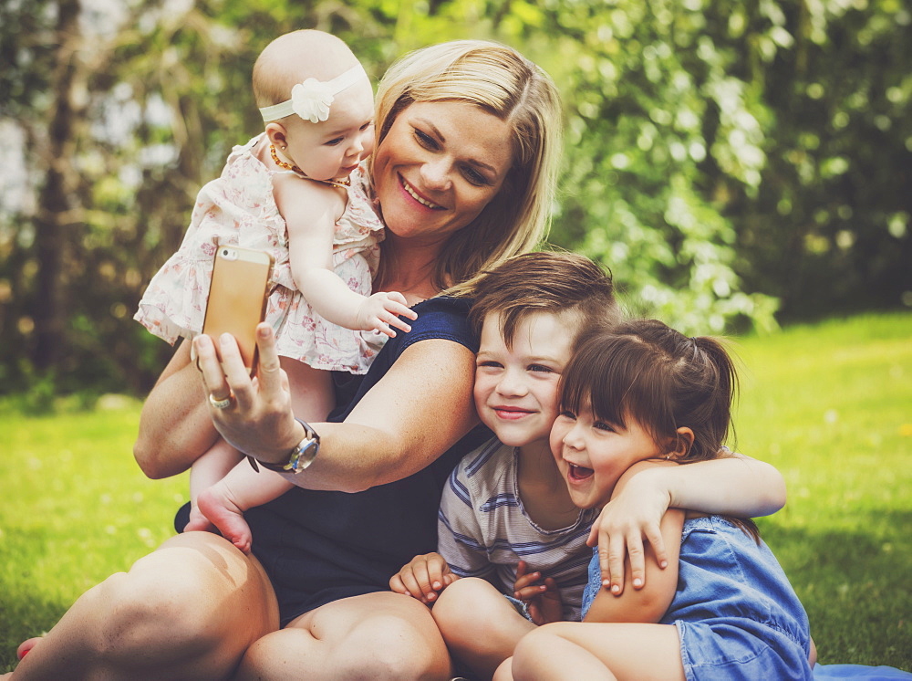 A young mother taking a self-portrait with her kids in a park with the image having a vintage effect applied, Edmonton, Alberta, Canada