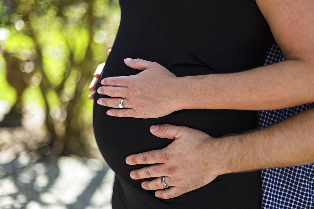 A couple expecting a baby, standing with hands on her pregnant belly, Surrey, British Columbia, Canada