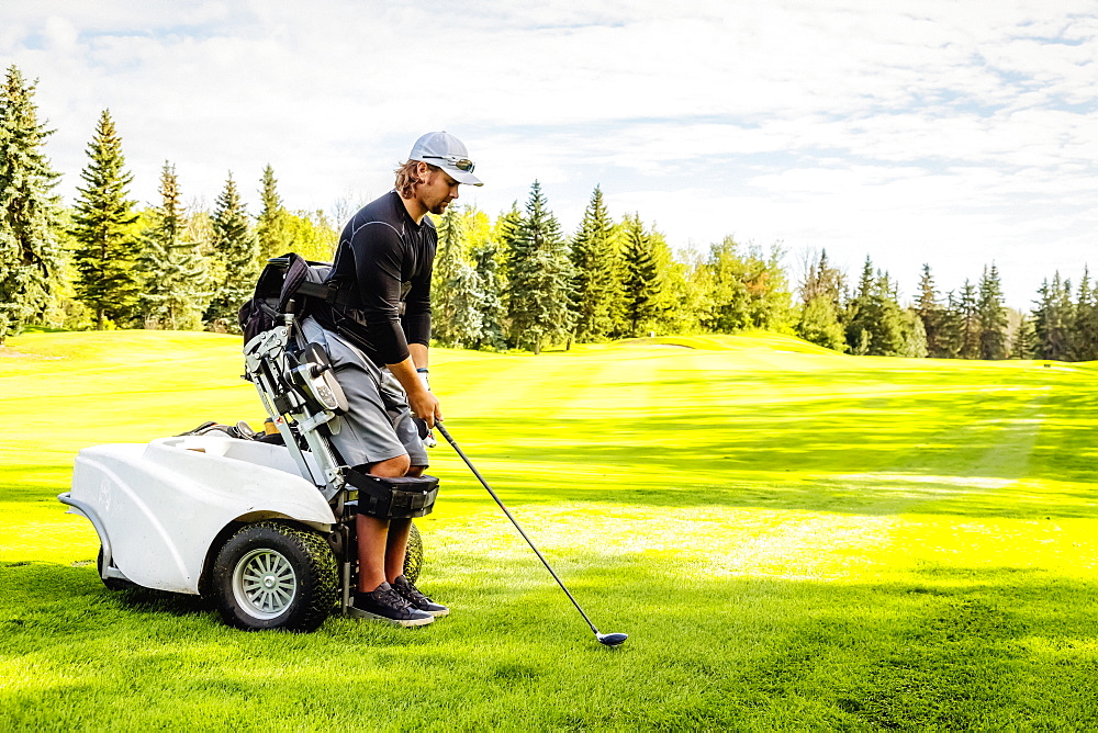 A physically disabled golfer using a specialized wheelchair lines up his driver with the ball on the golf green, Edmonton, Alberta, Canada