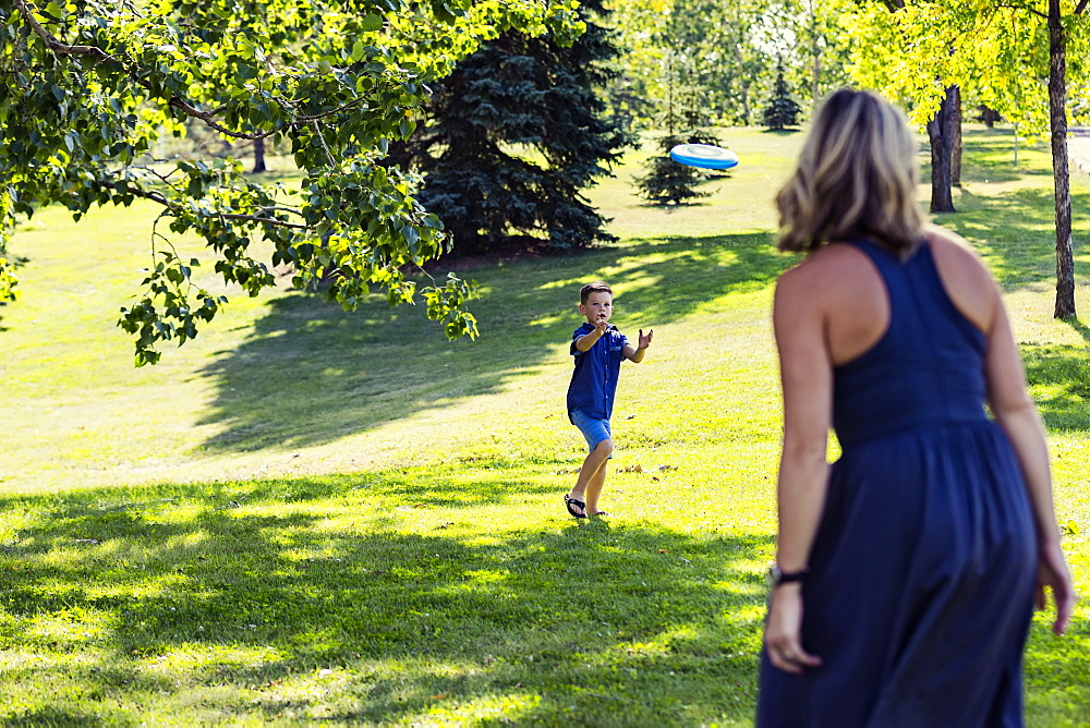 A mother throwing a disc toy to her son to catch in a park on warm fall afternoon during a family outing, Edmonton, Alberta, Canada