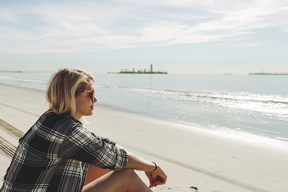 A woman sits on a beach looking out to the water, Long Beach, California, United States of America