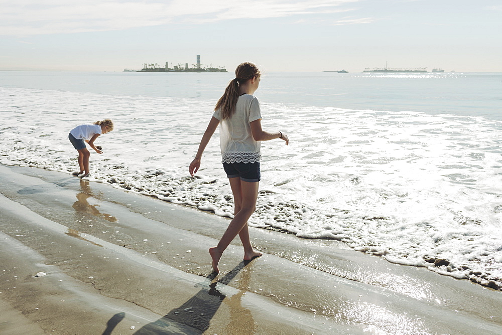 Two sisters walking out to the surf on a beach, Long Beach, California, United States of America