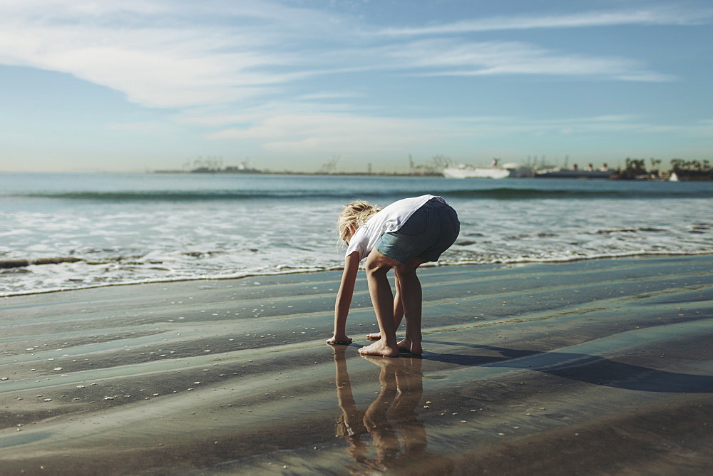 A young girl plays in the wet sand along the shoreline, Long Beach, California, United States of America