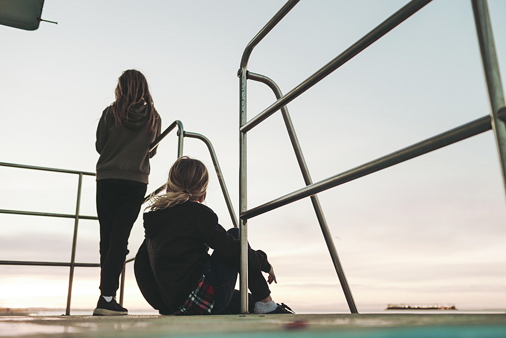 Two girls sit on a lifeguard station at dawn looking out to the ocean, Long Beach, California, United States of America