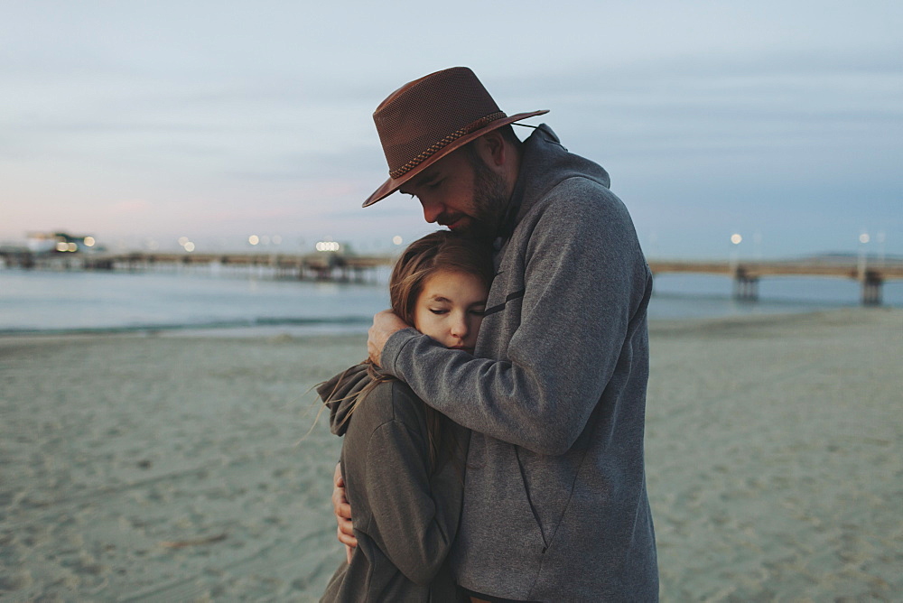 A father and daughter having a tender moment, the father holding his daughter in an embrace on a beach at dusk, Long Beach, California, United States of America