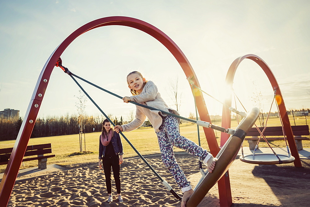 A young mom and her daughter playing on a saucer swing in a playground on a warm autumn evening, Edmonton, Alberta, Canada