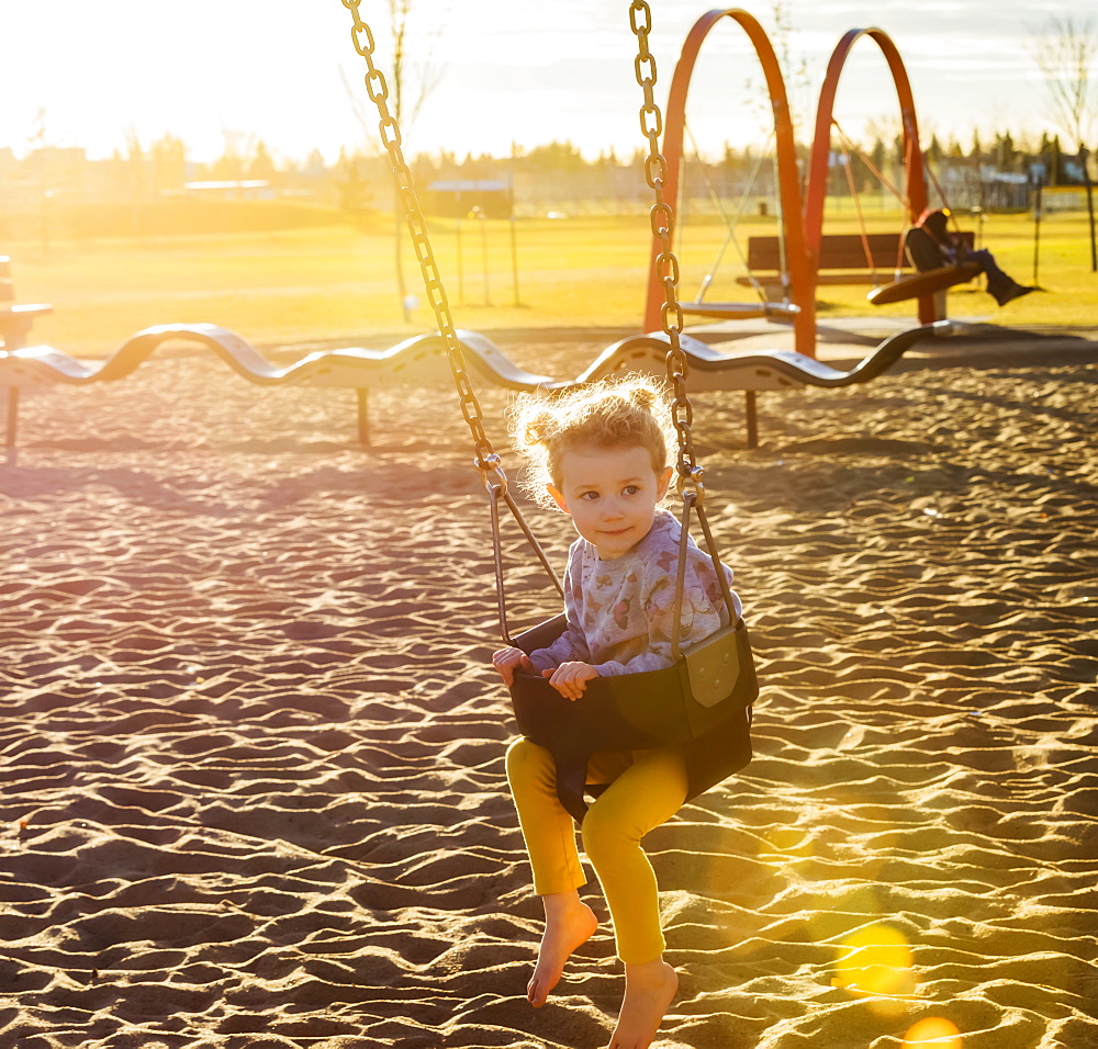 A young girl swinging by herself in a playground and enjoying a warm fall evening, Edmonton, Alberta, Canada