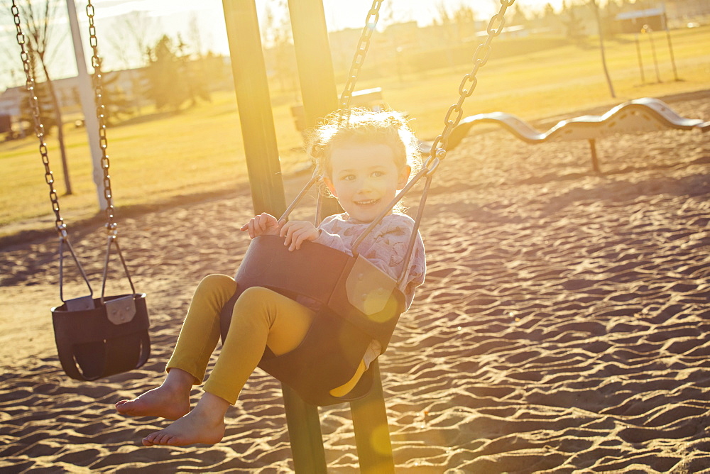 A young girl swinging by herself in a playground and enjoying a warm fall evening, Edmonton, Alberta, Canada