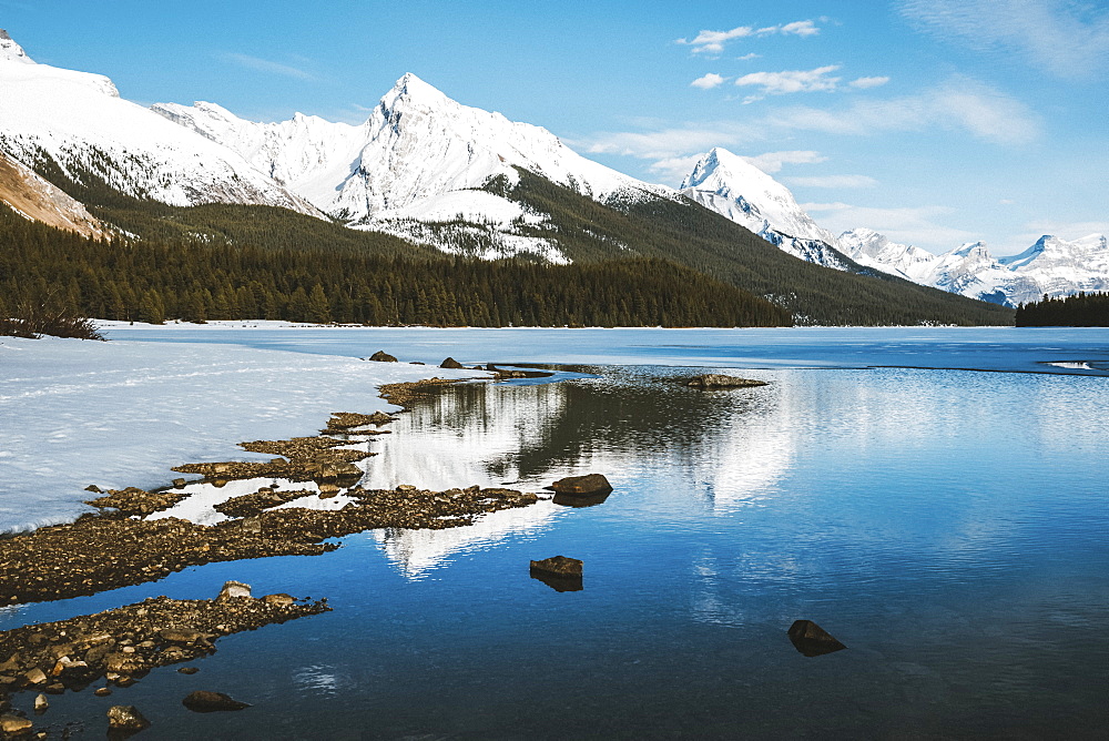 Thawing of a frozen lake and snow-capped rugged mountains peaks, Jasper National Park, Alberta, Canada