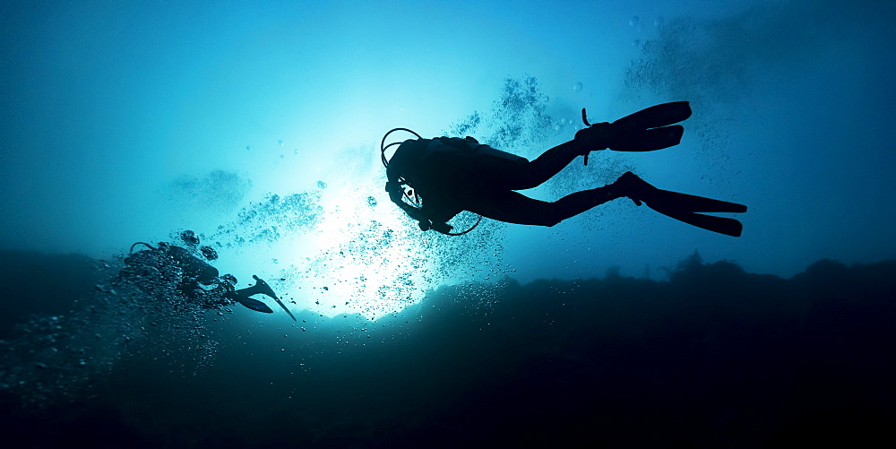 Scuba divers in the Great Blue Hole dive site on the Belize Barrier Reef. This site was made famous by Jacques Cousteau, who declared it one of the top five scuba diving sites in the world, Belize