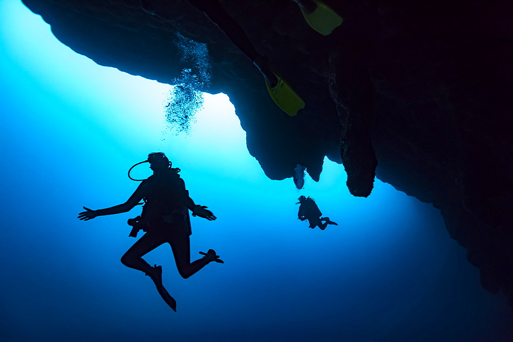 Scuba divers in the Great Blue Hole dive site on the Belize Barrier Reef. This site was made famous by Jacques Cousteau, who declared it one of the top five scuba diving sites in the world, Belize