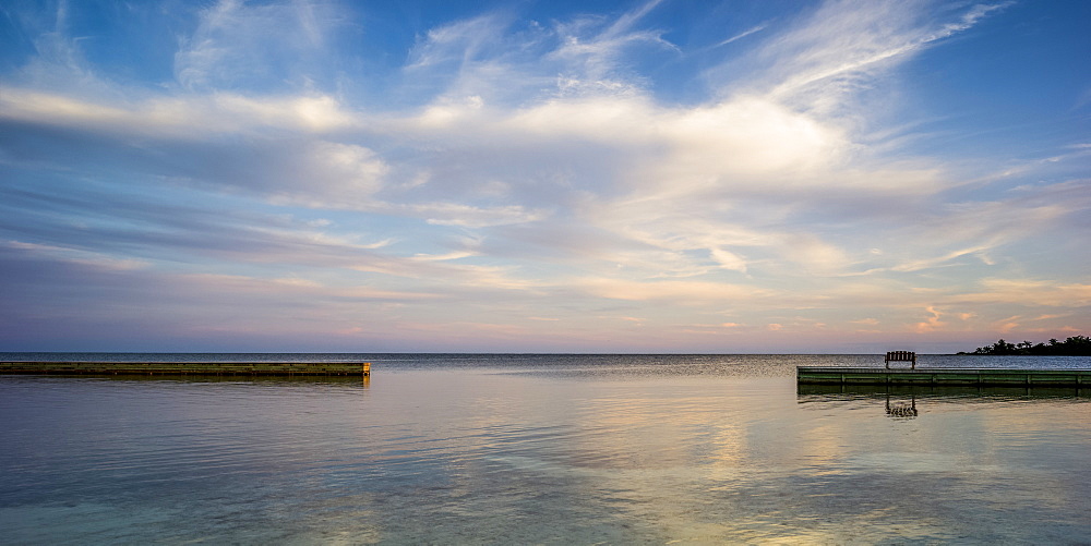 A wooden bench on a dock facing the coastline and open ocean at sunrise, Belize