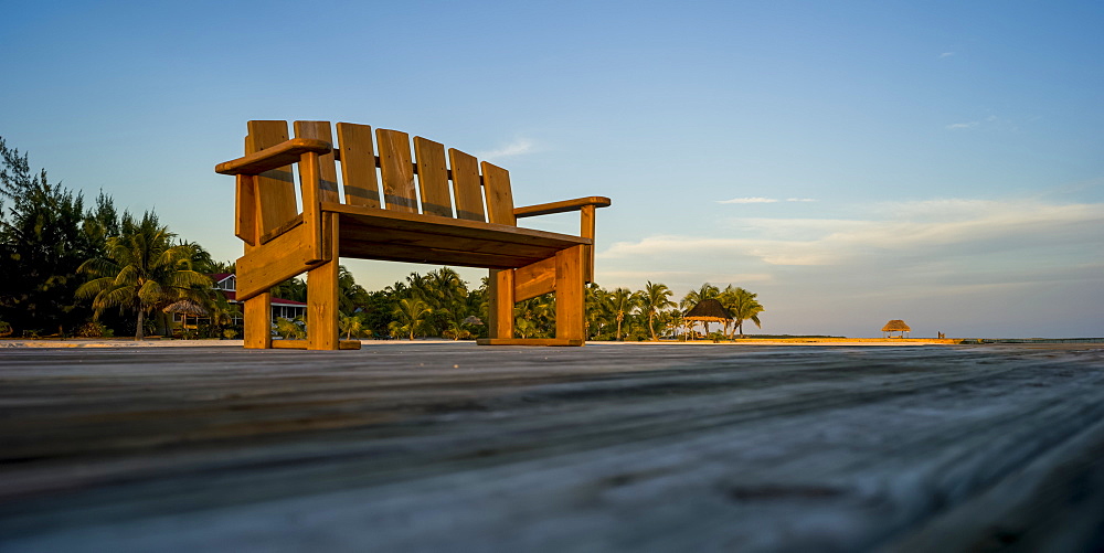 A wooden bench on a dock with palm trees along the coast, Belize