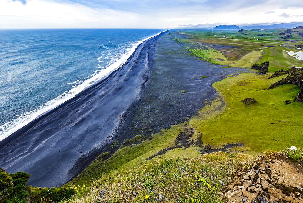 The view from the top of the tourist lookout at Dyrholaey near Vik, Southern Iceland. The black sand beach extends for miles into the distance and green pasture and farmland is seen in the background, Vik, Iceland