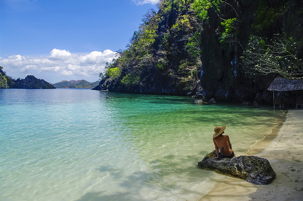 A woman in a bikini sits on a rock along a tropical coastline, Andaman Islands, India