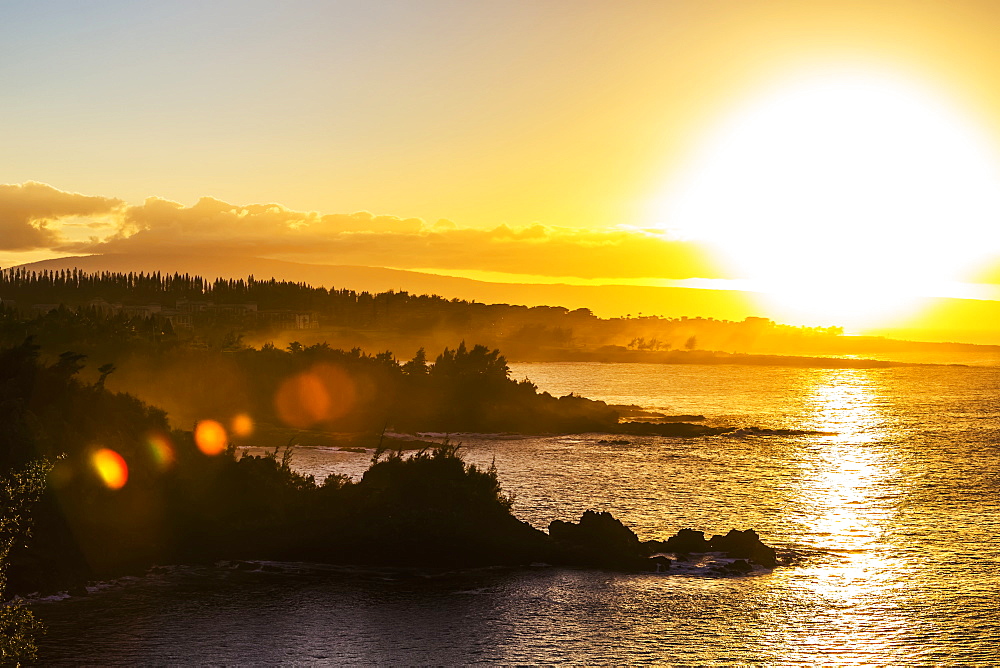 A golden sunset casting yellow light over the ocean and coastline near Honolua Bay, Kaanapali, Maui, Hawaii, United States of America