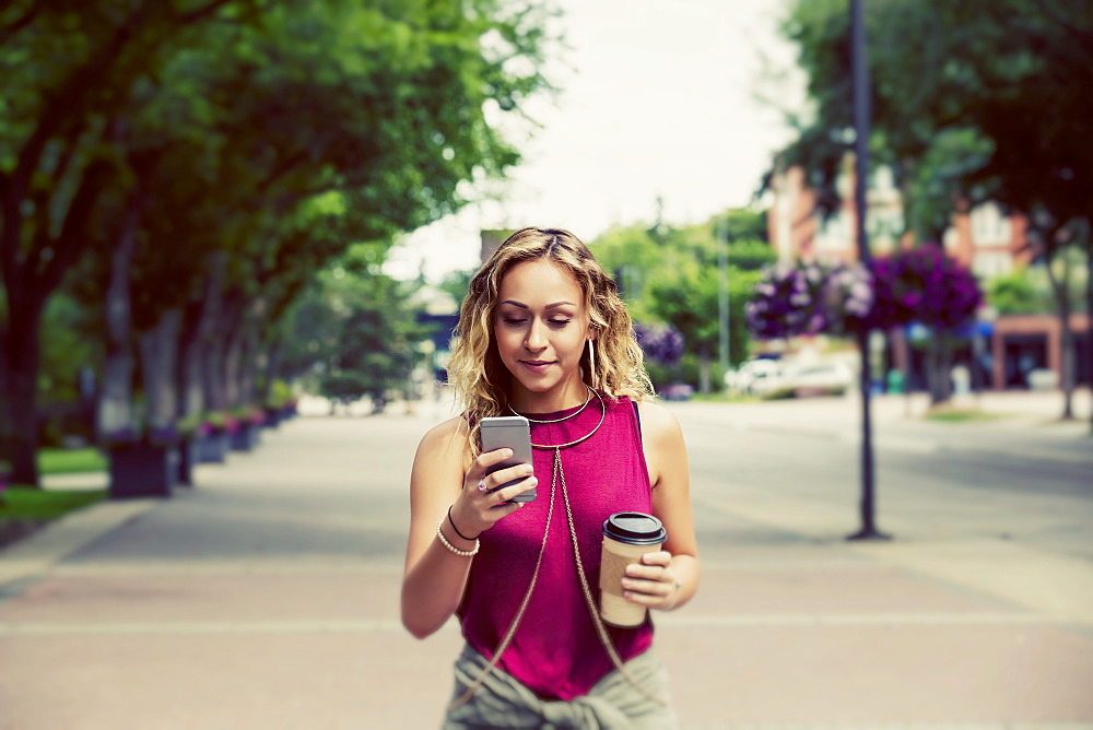 A beautiful young woman walking down a street near a university campus texting on her smart phone, Edmonton, Alberta, Canada