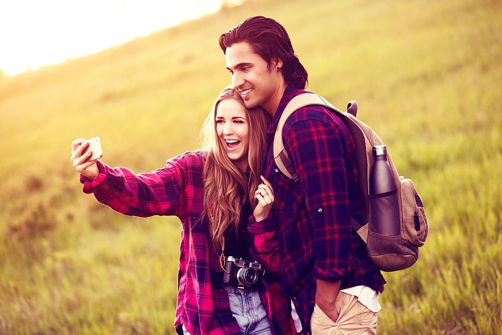 Young couple in a park posing for a self-portrait with their cell phone, Edmonton, Alberta, Canada