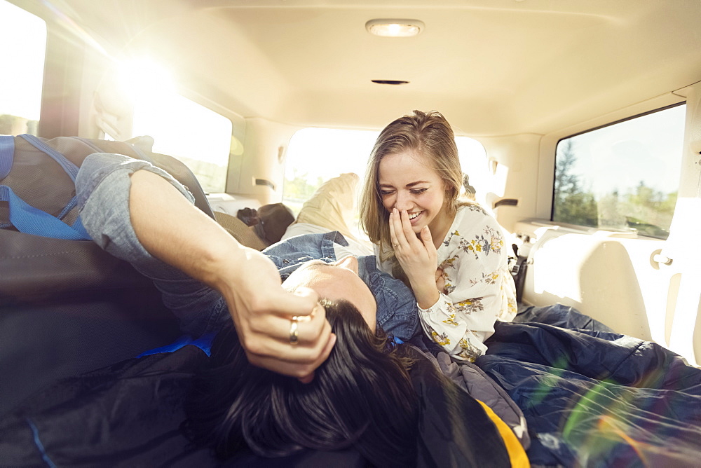 A young couple lays in the back of their vehicle during a road trip talking and laughing together, Edmonton, Alberta, Canada