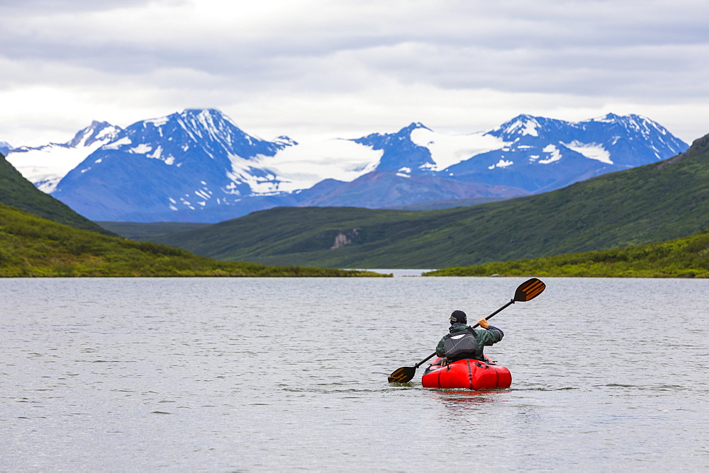 A man paddles a packraft across Landmark Gap Lake with the Alaska Range in the distance, Alaska, United States of America