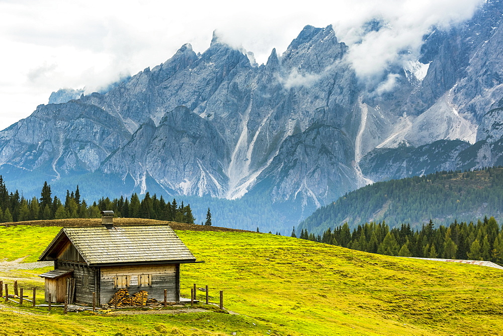 Wooden barn on top of alpine meadow with rugged mountain range in the background, Sesto, Bolzano, Italy