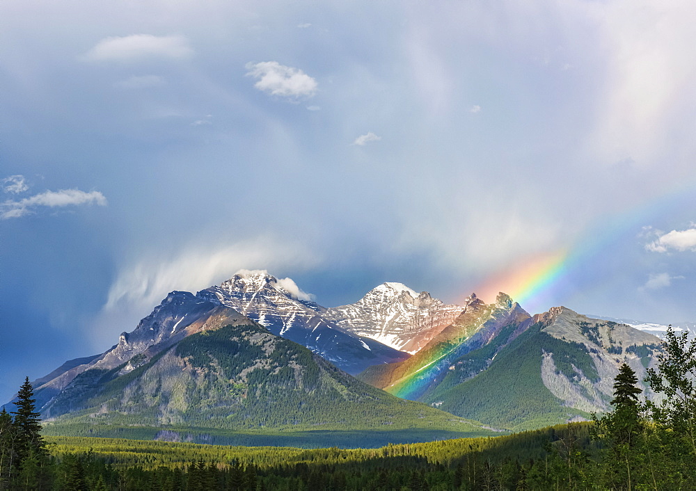 A rainbow emerges between rugged mountain peaks during a heavy rain storm, Banff, Alberta, Canada