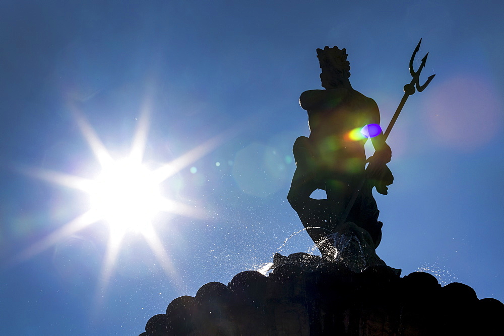 Silhouette of statue on top of fountain with sunburst and blue sky, Trento, Trento, Italy