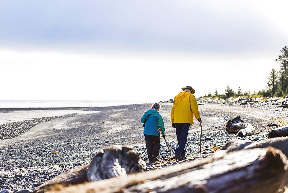 A senior couple hiking with walking sticks on the beach along the coast, Meadow Mist Campground, Graham Island, Tlell, Haida Gwaii, British Columbia, Canada