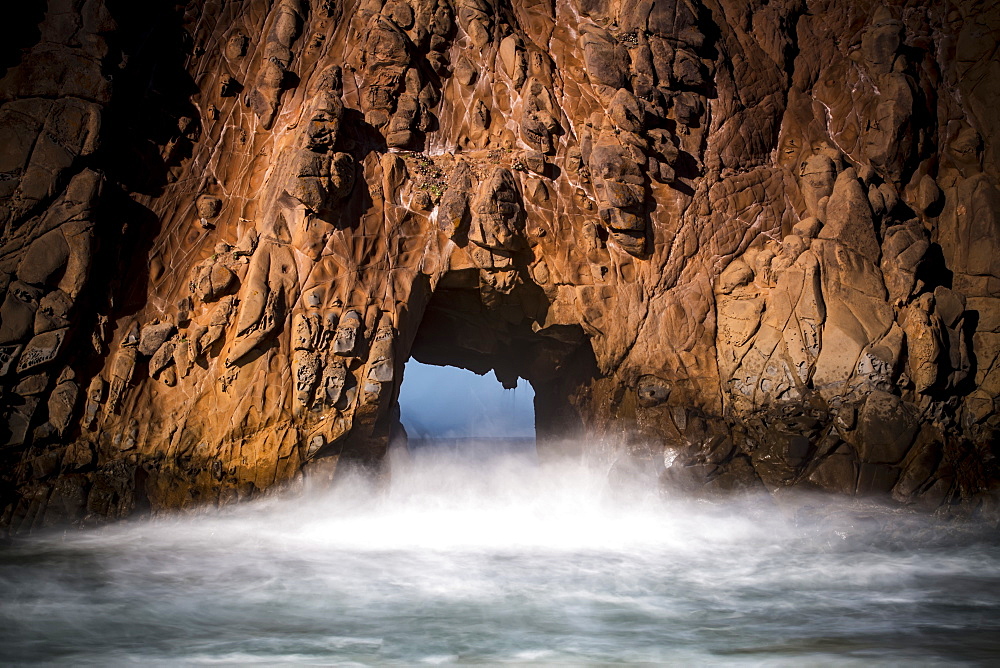 A natural arch in the rock formation along the coast with mist rising off the water, Big Sur, California, United States of America