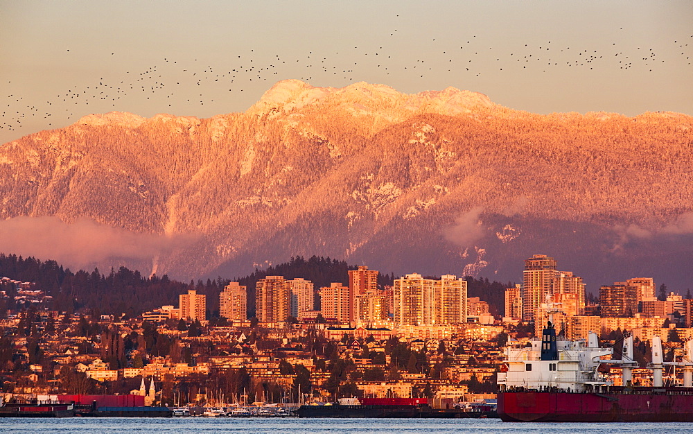 The North Vancouver skyline and Coast Mountains glowing at dusk and ships in the harbour, Vancouver, British Columbia, Canada