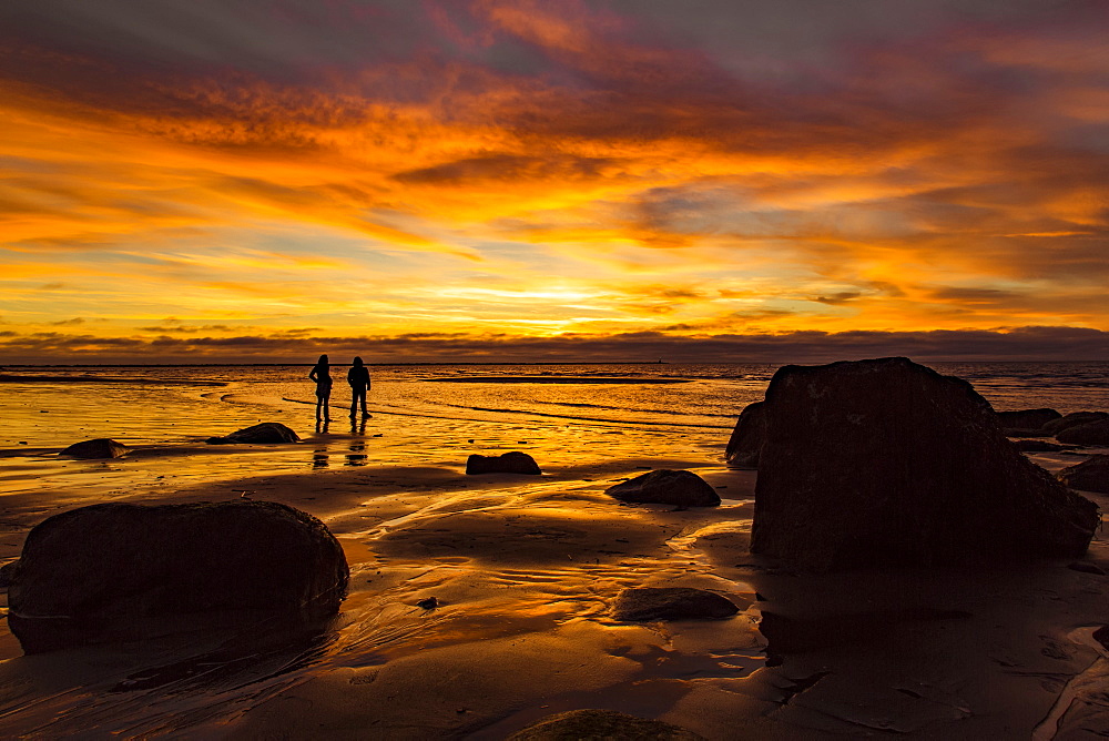 Silhouette of two people standing on Wreck Beach with an orange glow at sunset, Vancouver, British Columbia, Canada