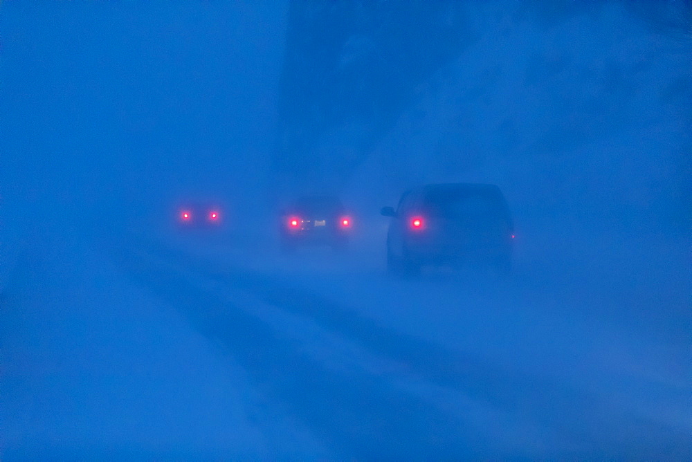 Car tail lights illuminate the blowing snow on the Seward Highway during a dark, winter night, Turnagain Arm, Kenai Peninsula, South-central Alaska, Alaska, United States of America