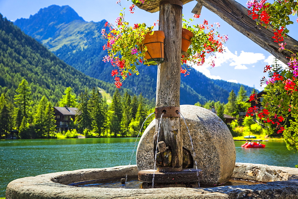 Close-up of a stone fountain with flower pots by Champex Lake and mountain range in the background, Champex, Valais, Switzerland