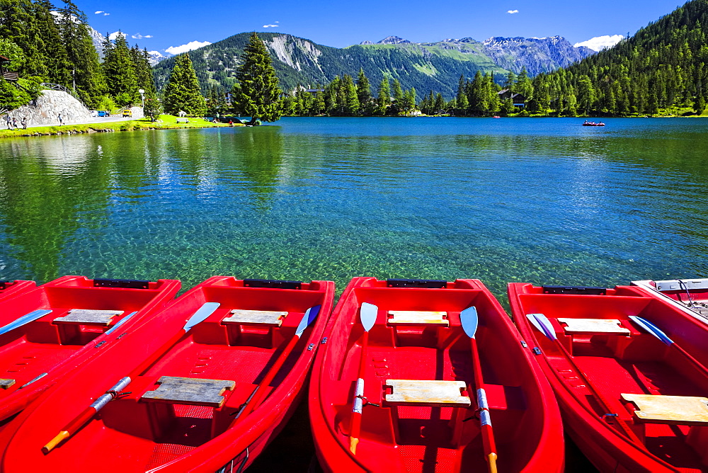 Red boats lined up at Champex Lake under blue sky with a mountain range in the background, Champex, Valais, Switzerland