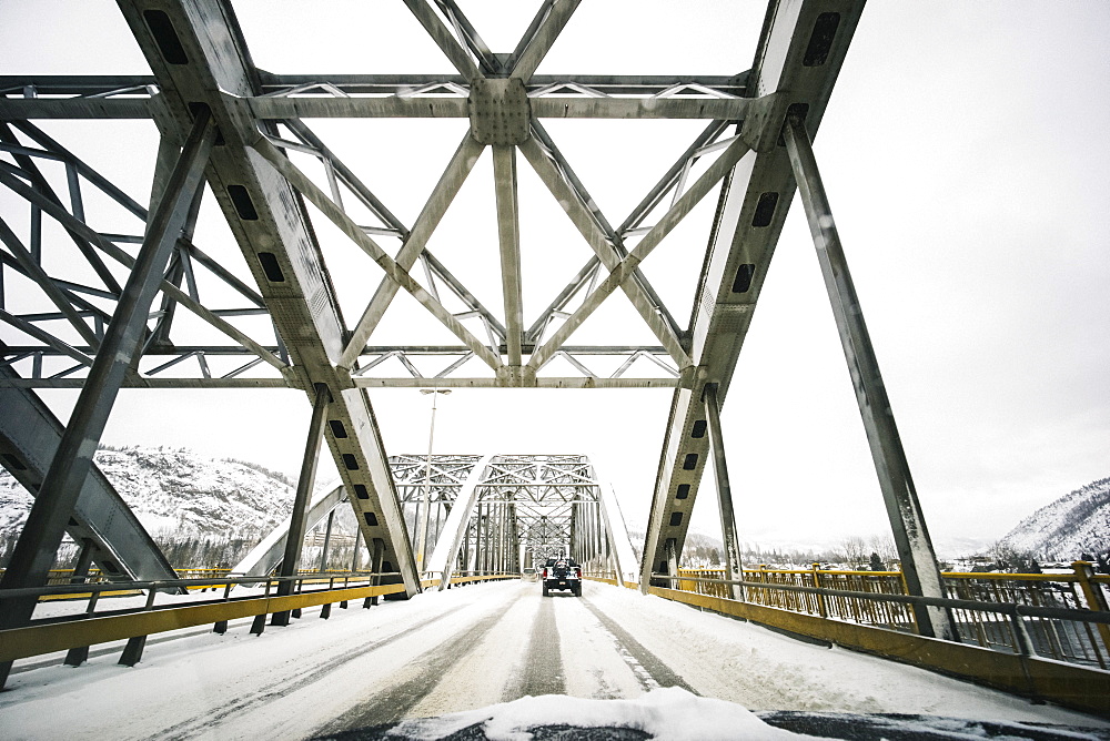 Vehicles traveling on a snow covered road over a bridge with a view from the front of a vehicle, Nelson, British Columbia, Canada