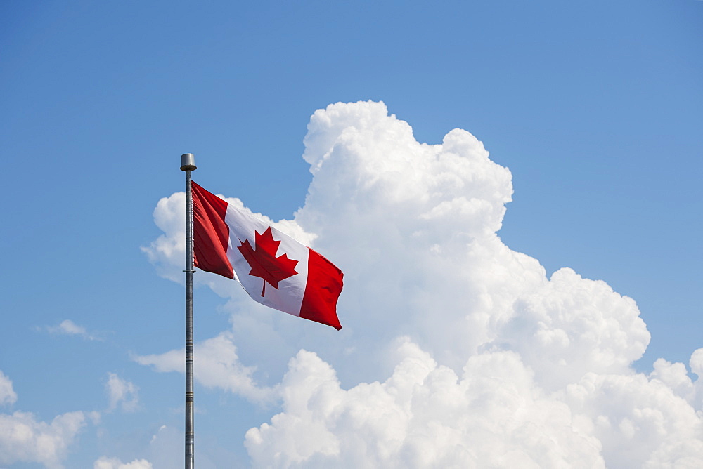 A Canada flag flying in a blue sky with cloud, Prince Edward Island, Canada