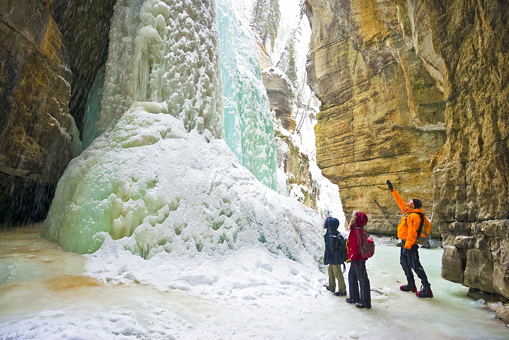 Three people viewing a large frozen canyon waterfall, Jasper National Park, Alberta, Canada