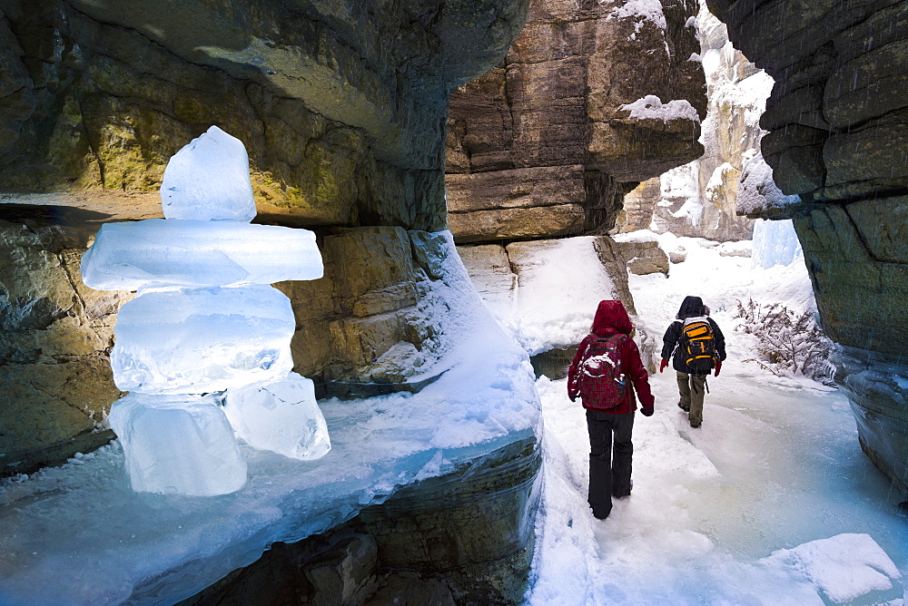 Two people exploring a canyon with ice block inukshuk in winter, Jasper National Park, Alberta, Canada