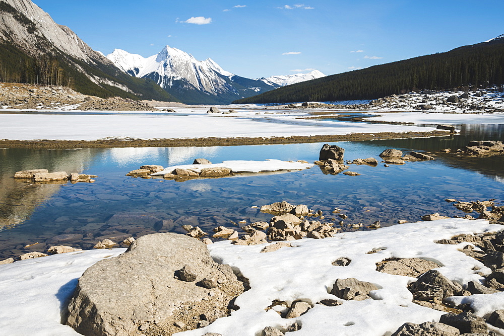 Snow on the lake and snow-capped rugged mountains peaks in Jasper National Park, Alberta, Canada