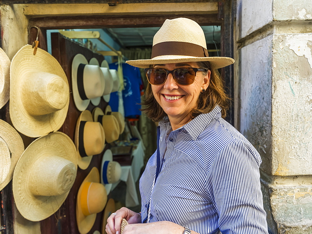 Female tourist looks at the camera and tries on a hat in a hat shop, Havana, Cuba