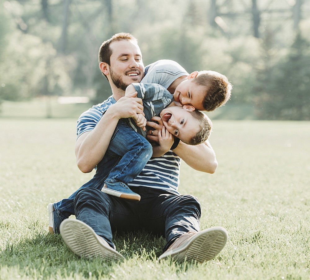 A father plays with his young sons on the grass in a park, Edmonton, Alberta, Canada