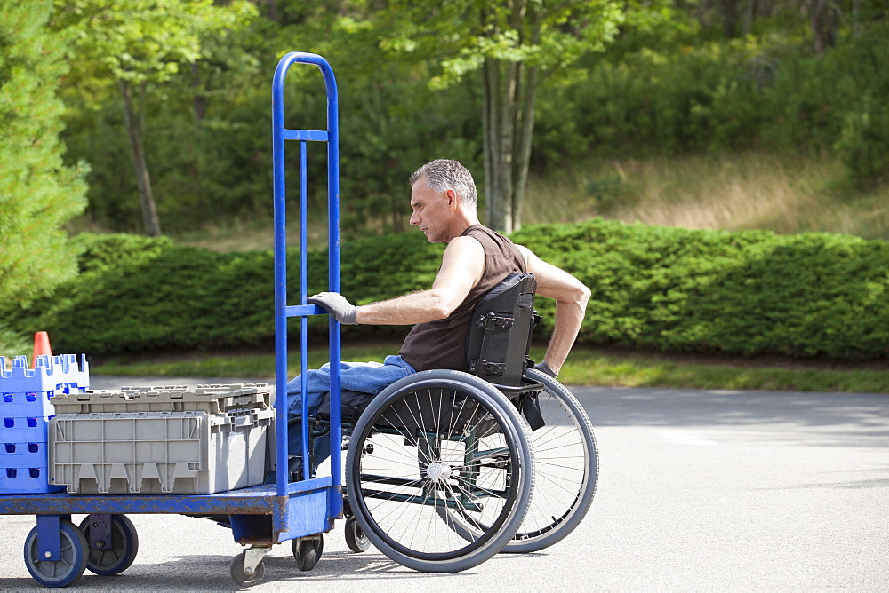 Loading dock worker with spinal cord injury in a wheelchair moving a hand truck