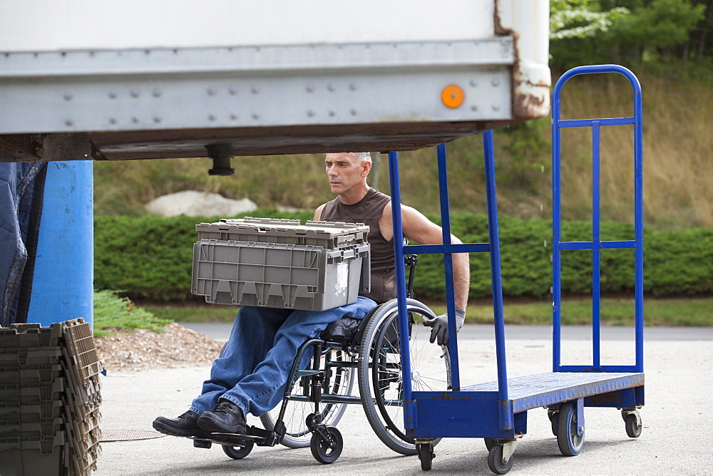 Loading dock worker with spinal cord injury in a wheelchair moving stacked inventory trays