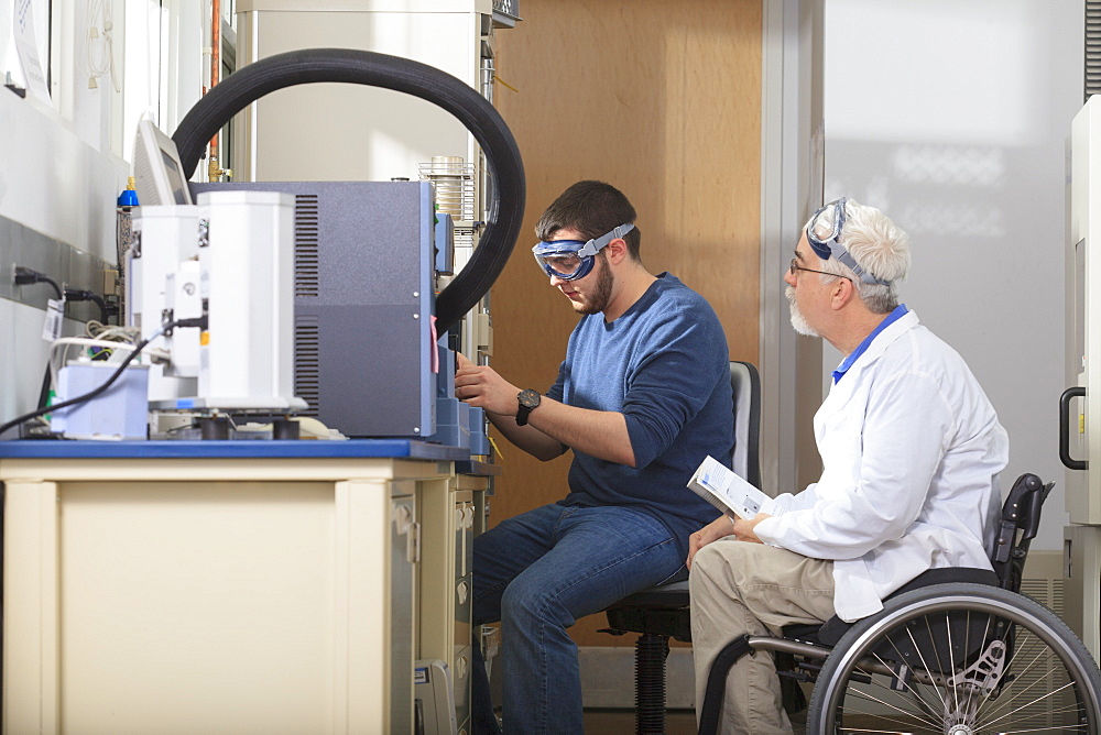 Professor with muscular dystrophy and engineering student using the thermogravimetric analyzer in a laboratory