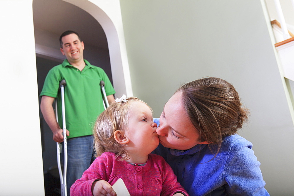 Man after anterior cruciate ligament (ACL) surgery with his wife kissing her daughter at home