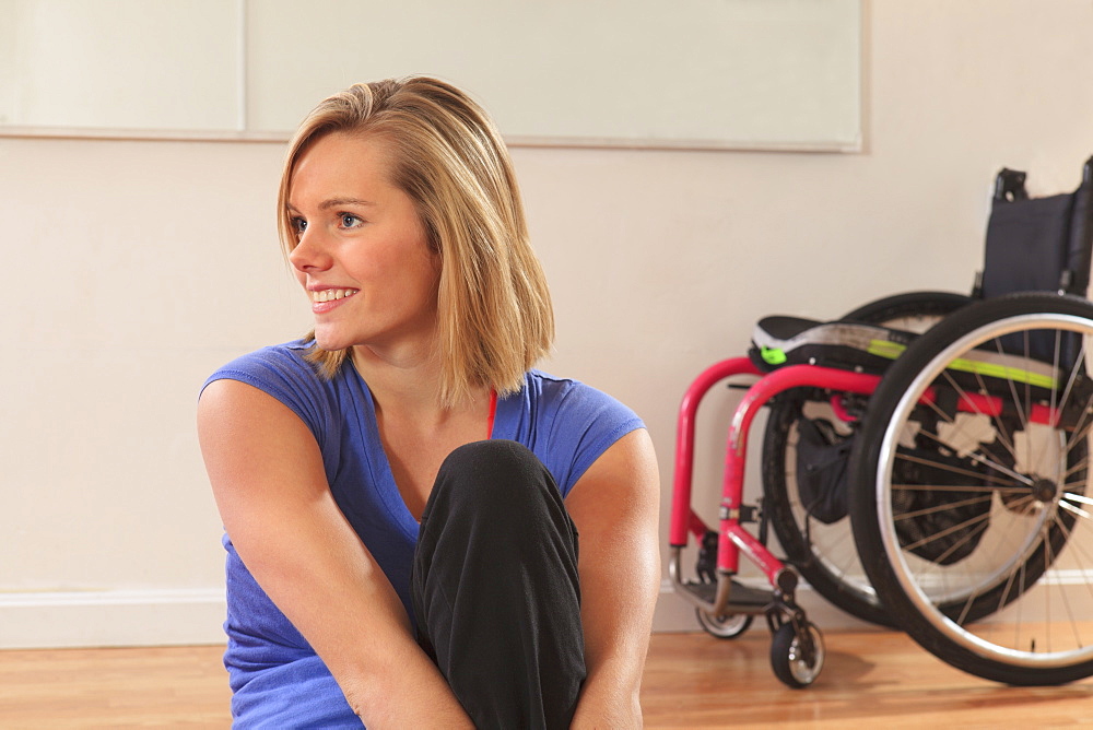 Portrait of a young woman with a spinal cord injury and her wheelchair in a yoga studio