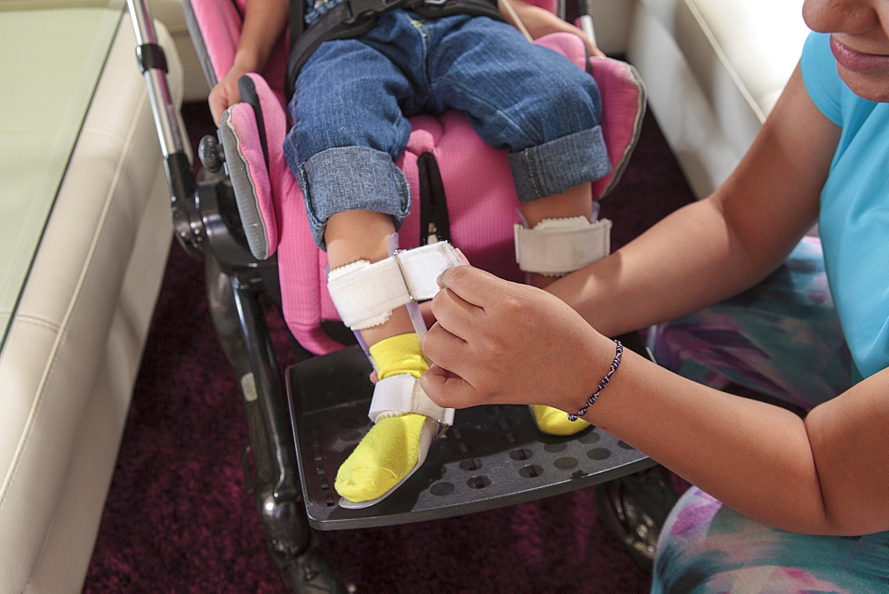 Mother putting leg brace on small daughter with Cerebral Palsy