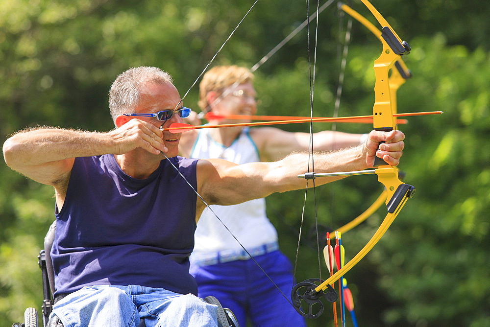 Man with spinal cord injury and woman with prosthetic leg aiming arrows at target